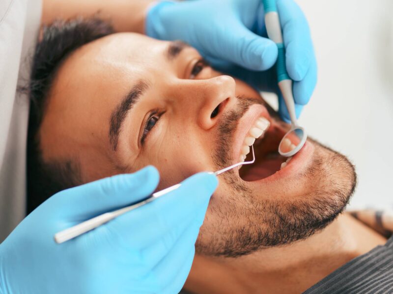 Joven con periodoncia sentado en la silla del dentista mientras el médico examina sus dientes